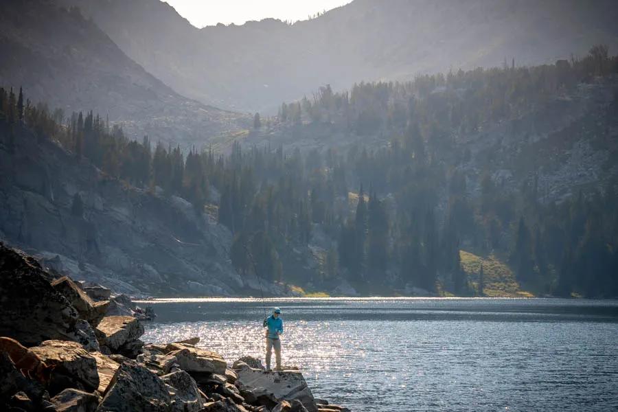 A fly fisher casts on a mountain lake Casting beneath the shadow of towering peaks for native trout in remote country is a pinnacle experience for any angler