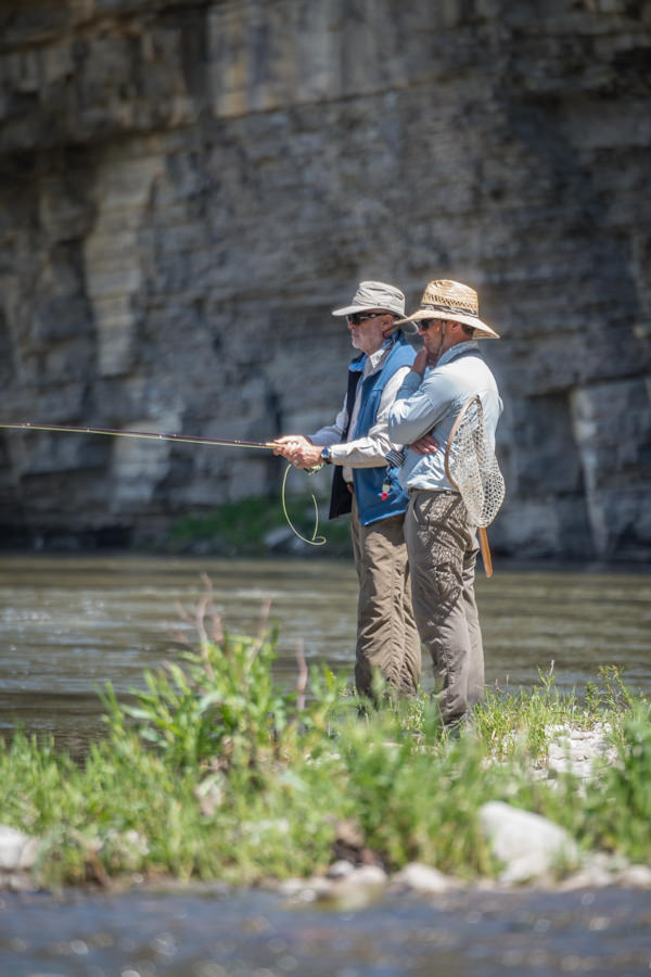 Man wearing a cowboy hat while fly fishing in a river in the